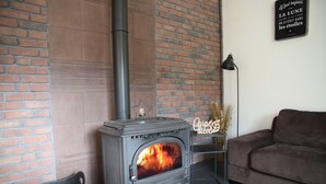 Un salon moderne avec un poêle à bois, un mur en briques, une étagère en métal noir et un canapé marron.