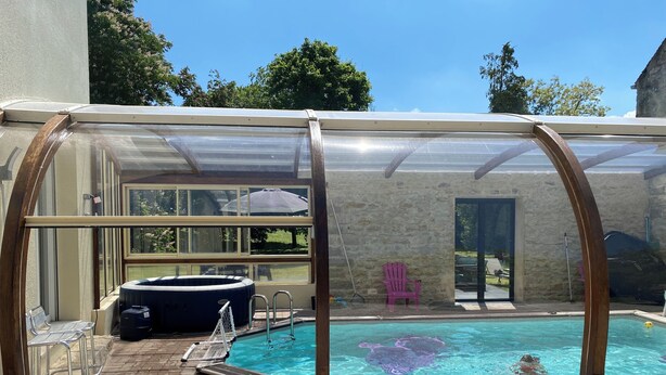 Une piscine couverte avec un jacuzzi, un espace patio doté de chaises et un mur de pierre en arrière-plan.