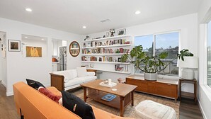 A modern living room with a white sofa, a wooden coffee table, a bookshelf, and a large window. - Modern Peaceful Tucked Away With Private Office (San Diego)