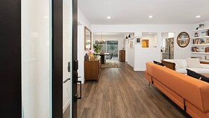 A modern living room with a sofa, a dining area, and a kitchen visible through an open doorway. - Modern Peaceful Tucked Away With Private Office (San Diego)