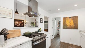 A modern kitchen with white cabinetry, a stainless steel range, and a large painting on the wall. - Modern Peaceful Tucked Away With Private Office (San Diego)