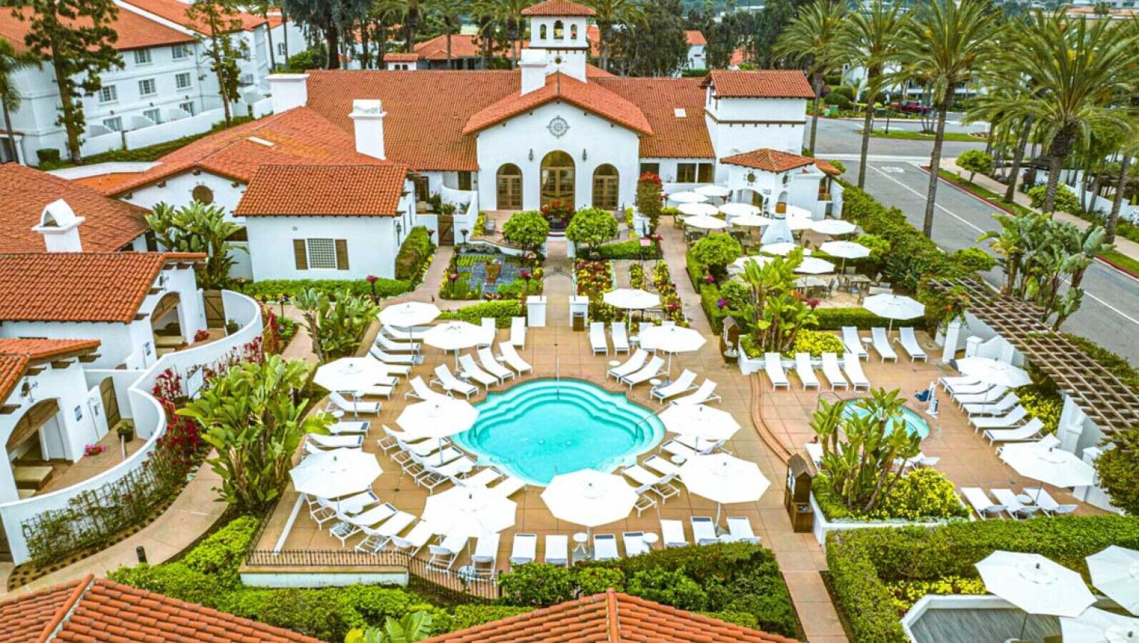 A resort with a central swimming pool, lounge areas, and a white building with a red-tiled roof.