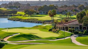 A golf course with a clubhouse, a lake, and a hilly landscape. - On Omni La Costa Golf Course- Patio, Parking, & AC (Carlsbad)