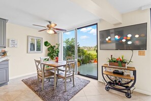 Una cocina moderna con una mesa de comedor, sillas, un ventilador de techo, un televisor y una puerta corrediza de vidrio que da a un jardín.