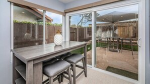 A patio area with a table and chairs, a glass door leading outside, and a wooden fence in the background.
