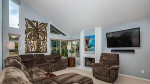 A spacious living room with a large sectional sofa, a fireplace, a flat-screen TV, and a large decorative wall piece.