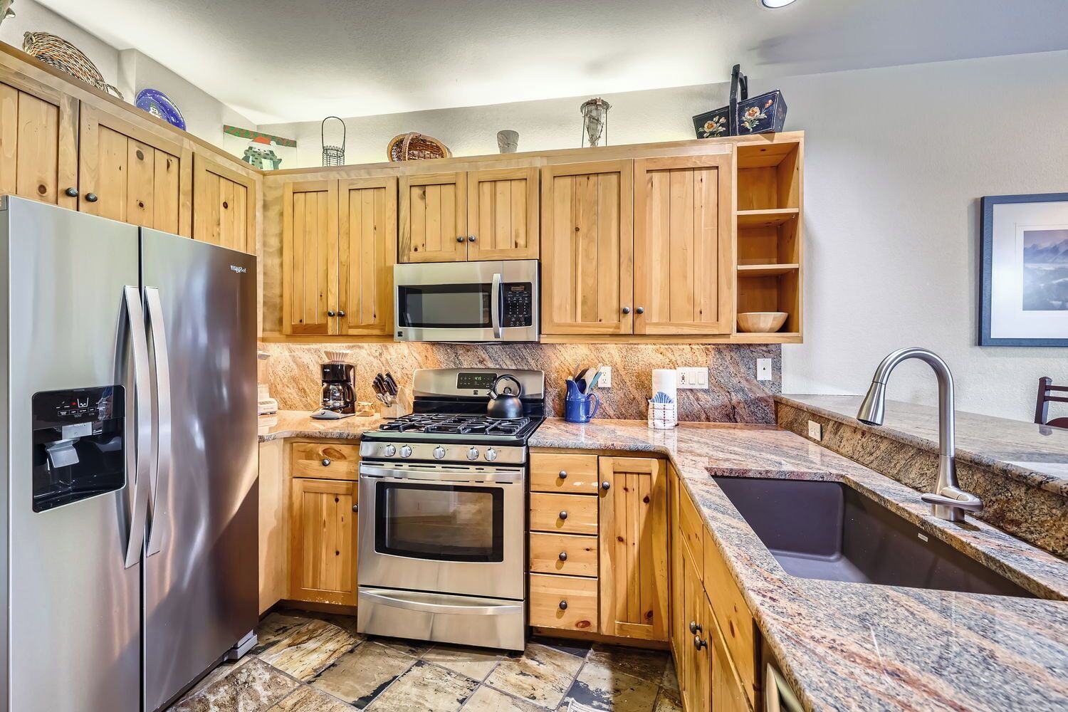 A modern kitchen with wooden cabinets, stainless steel appliances, granite countertops, and a built-in microwave.