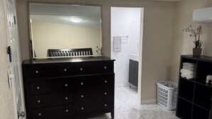 A bedroom with a bed, a dresser, a mirror, a laundry basket, and a shelf with towels. - Cozy 2-bedroom apartment 3 mins away from
Tampa Int’l airport  (Tampa)