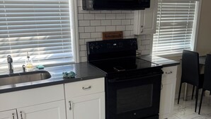 A kitchen with white cabinets, a black stove, a microwave, and a sink. - Cozy 2-bedroom apartment 3 mins away from
Tampa Int’l airport  (Tampa)
