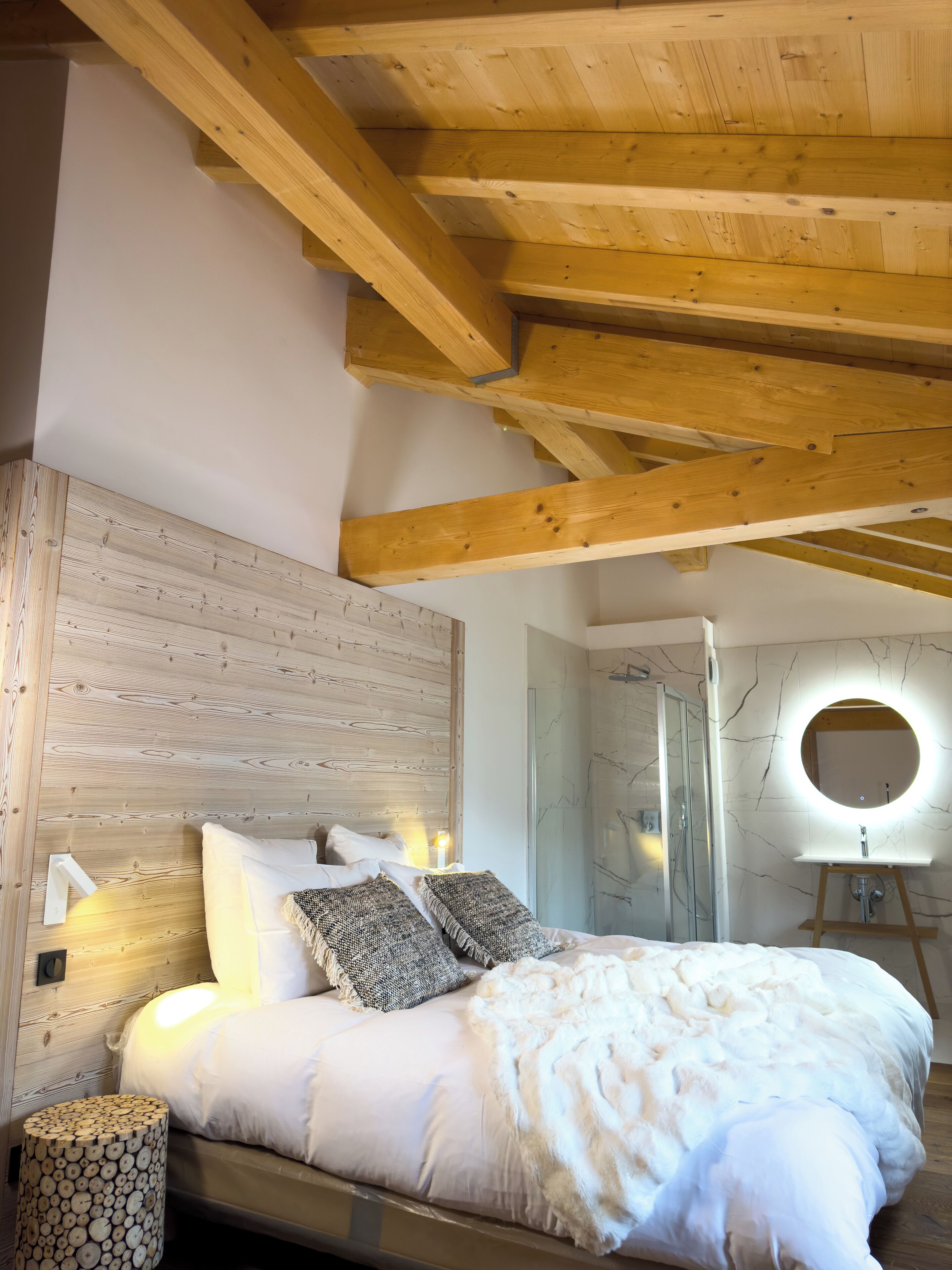 Ein Schlafzimmer mit Holzbalkendecke, einem Bett mit weißer Bettwäsche, einem runden Spiegel über dem Bett und einem Nachttisch aus Holz.