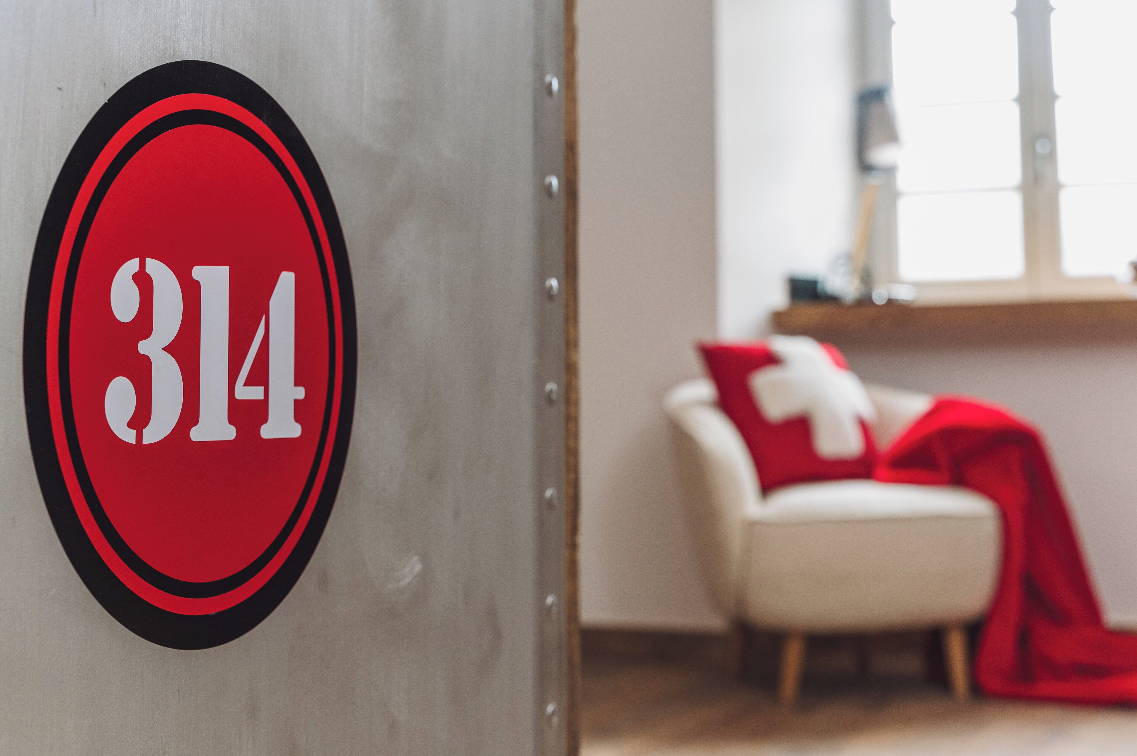 Quarto com uma porta identificada com o número '314' e uma cadeira branca com manta vermelha.