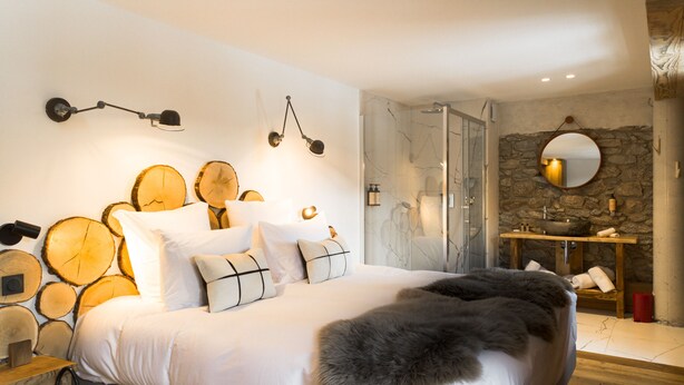 A bedroom with a large bed, wooden wall decor, a stone wall, a mirror, and a wooden nightstand. - Grand Hôtel l'Ermitage Font-Romeu - Handwritten Collection (Font-Romeu-Odeillo-Via)