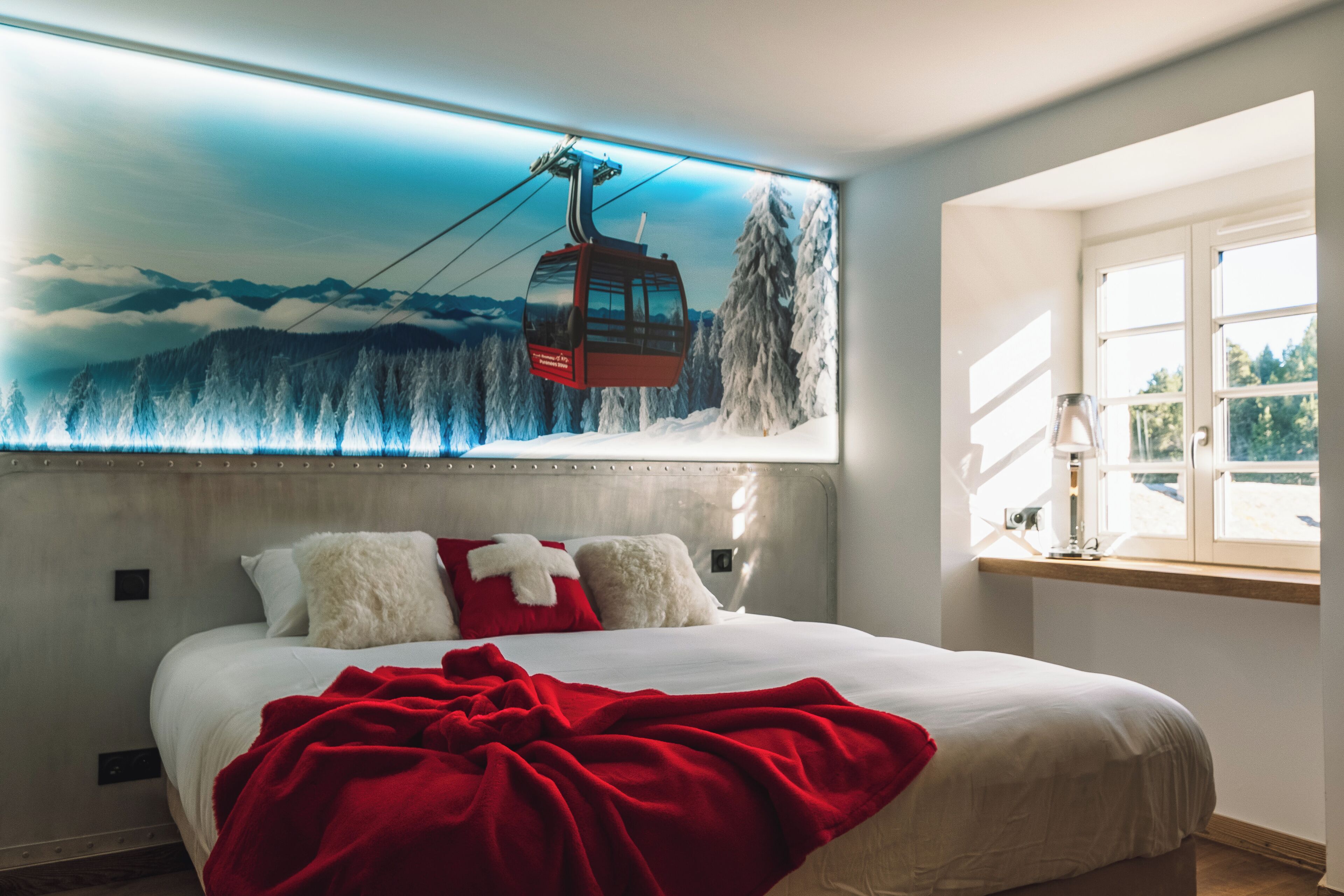 Habitación de hotel con una cama grande, un mural con temática de telesilla en la pared y una ventana con vistas al exterior.