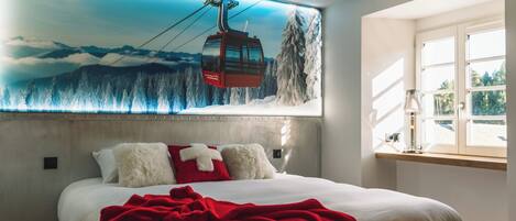 Ein Hotelzimmer mit einem großen Bett, einem Wandgemälde mit einer Seilbahn und einem Fenster mit Blick ins Freie.