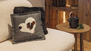 A cozy room with a wooden wall, a window, a shelf with decorative items, a small table with a teapot, and a plush sofa with heart-shaped cushions. - Grand Hôtel l'Ermitage Font-Romeu - Handwritten Collection (Font-Romeu-Odeillo-Via)