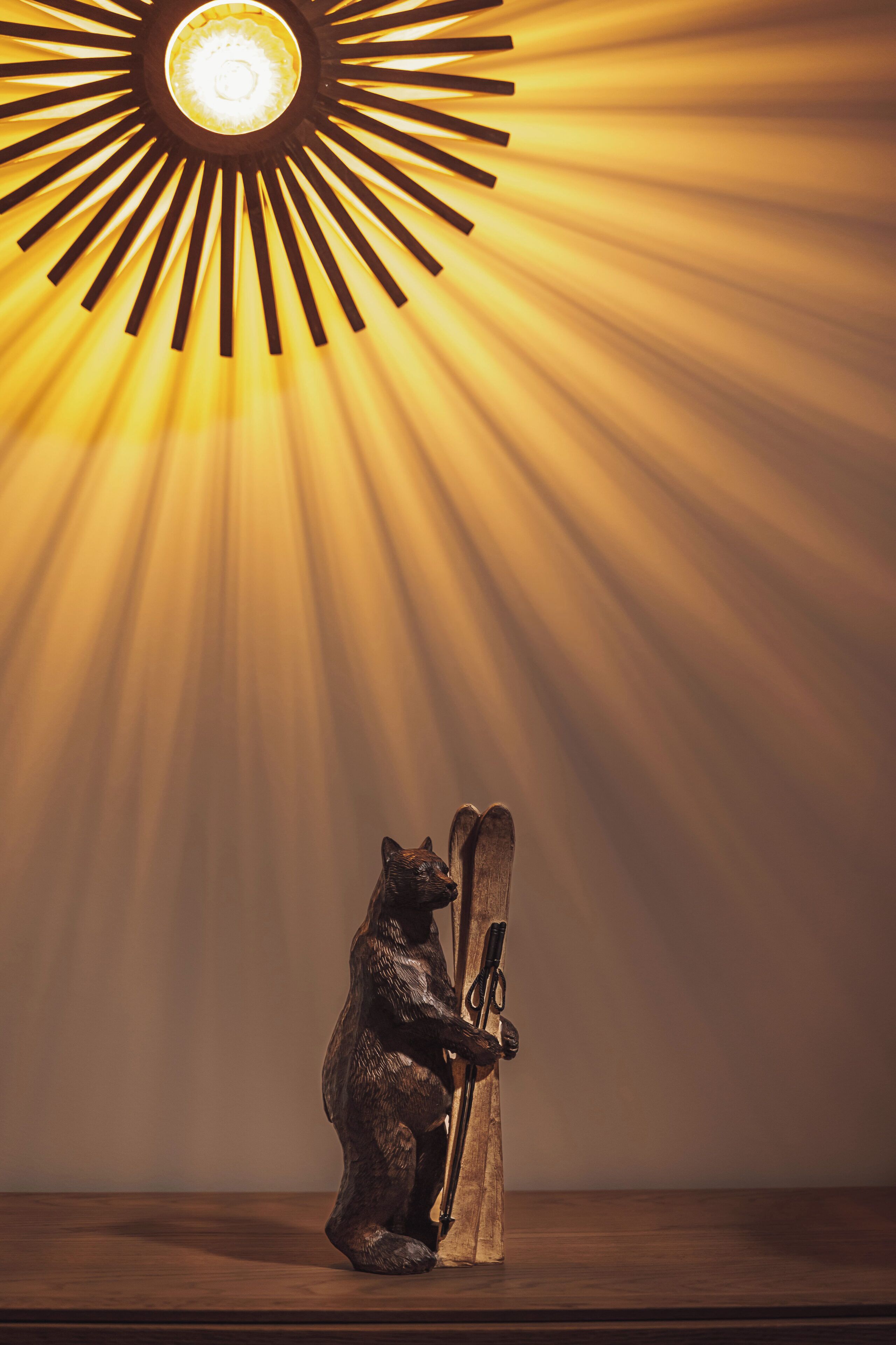 A bear sculpture holding a ski under a sunburst light fixture.