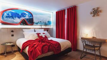 Une chambre à coucher avec un lit, une couverture rouge, un rideau rouge, un bureau avec une chaise et un élément de décoration fixé au mur.