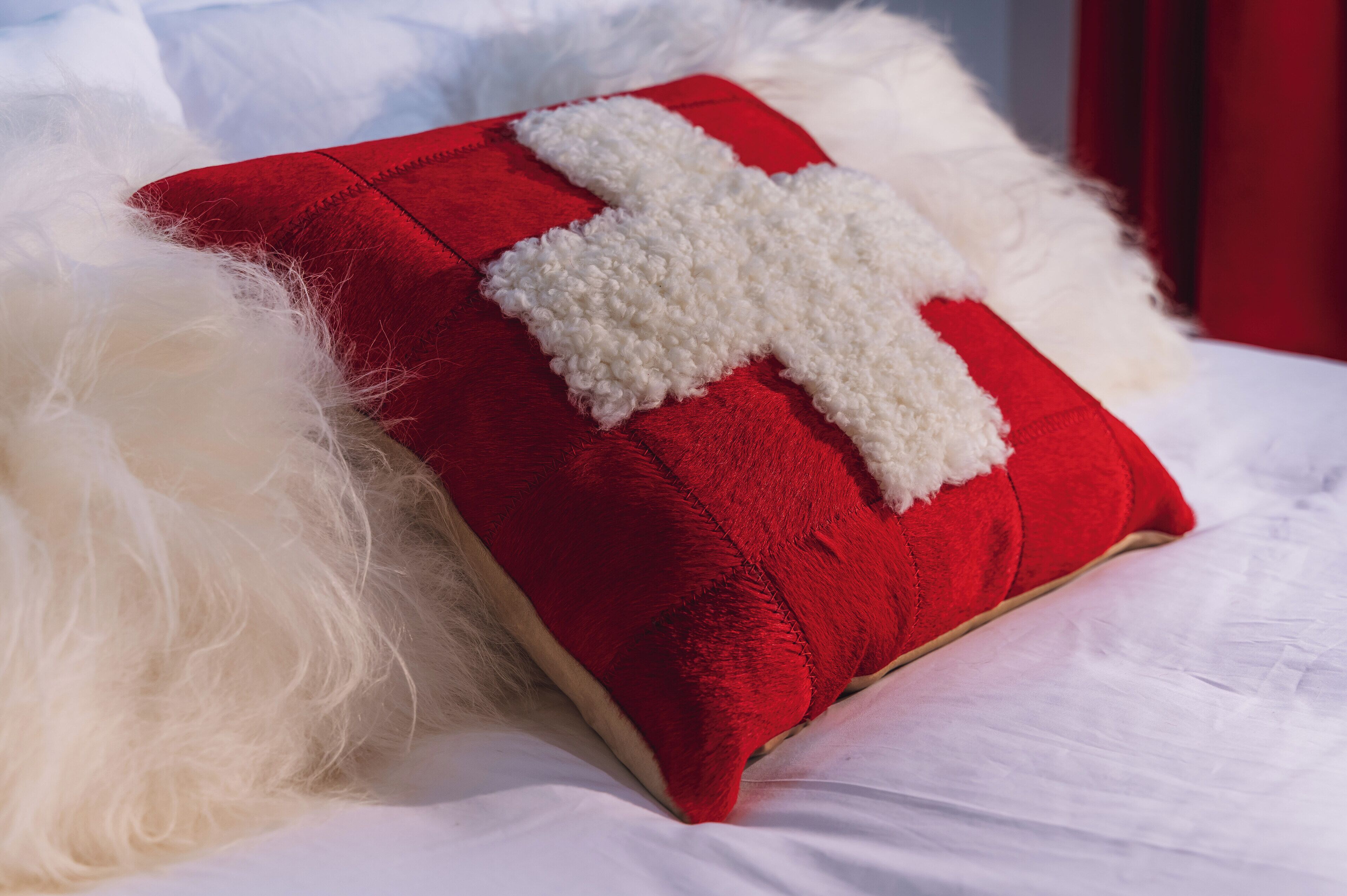 A bed with a red pillow and a white fluffy pillow.