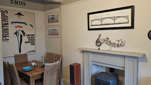 A dining area with wicker chairs, a wooden table, and a fireplace. - Snug - Macushla Apartment (Helensburgh)