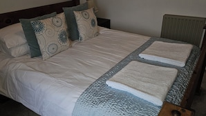 A neatly made bed with a white duvet, two pillows with a floral pattern, and two folded towels on the bed. - Snug - Macushla Apartment (Helensburgh)