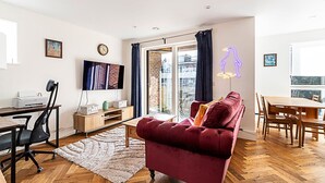 A modern living room with a red sofa, wooden dining table, and a TV mounted on the wall.