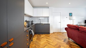 A modern kitchen with grey cabinets, a herringbone wooden floor, and a red sofa in the living area.