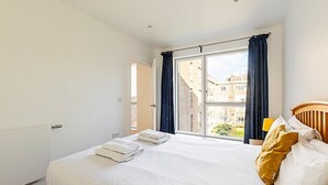 A hotel room with a large bed, a view of the city through a window, and a wooden headboard.