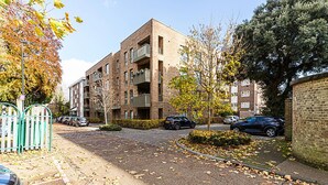 A multi-story residential building with balconies, a gated driveway, and parked cars.