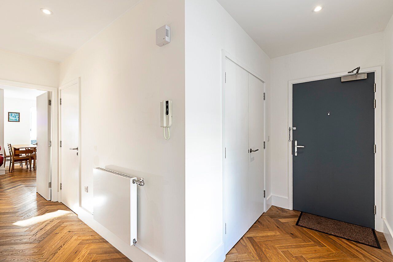 A hallway with a radiator, a door with a handle, and a dark-colored door with a peephole.