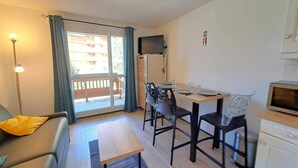 A compact living space with a sofa, a dining table with chairs, a kitchenette, and a sliding glass door leading to an outdoor area.
