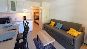 A compact living space with a kitchenette, a dining area, and a sofa with cushions.