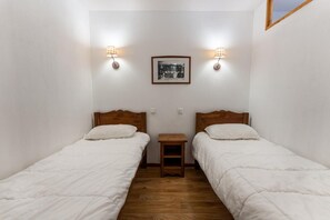 A small, clean room with two single beds, a wooden nightstand, and two wall-mounted lamps.