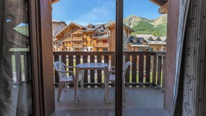 A wooden balcony with a table and chairs, overlooking a mountain landscape. - 40m from ski slopes, 3rd floor, view mountain, fitness, swimming pool, sauna, balcony, tv (Les Orres)