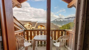 Un balcon avec une table et deux chaises, offrant une vue sur un paysage montagneux parsemé de bâtiments de style chalet.