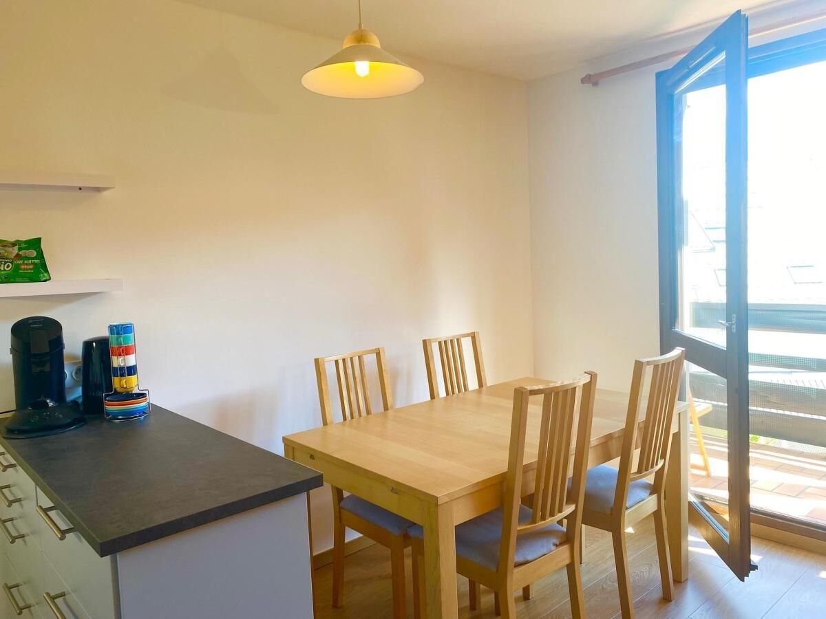 Un coin repas avec une table et des chaises en bois, un luminaire suspendu et une vue à travers une porte vitrée.