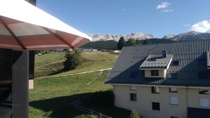 A building with a sloped roof and multiple windows, overlooking a grassy area with a mountain range in the background. - 5th floor, balcony, tv, 43m², Villard de Lans (Villard-de-Lans)