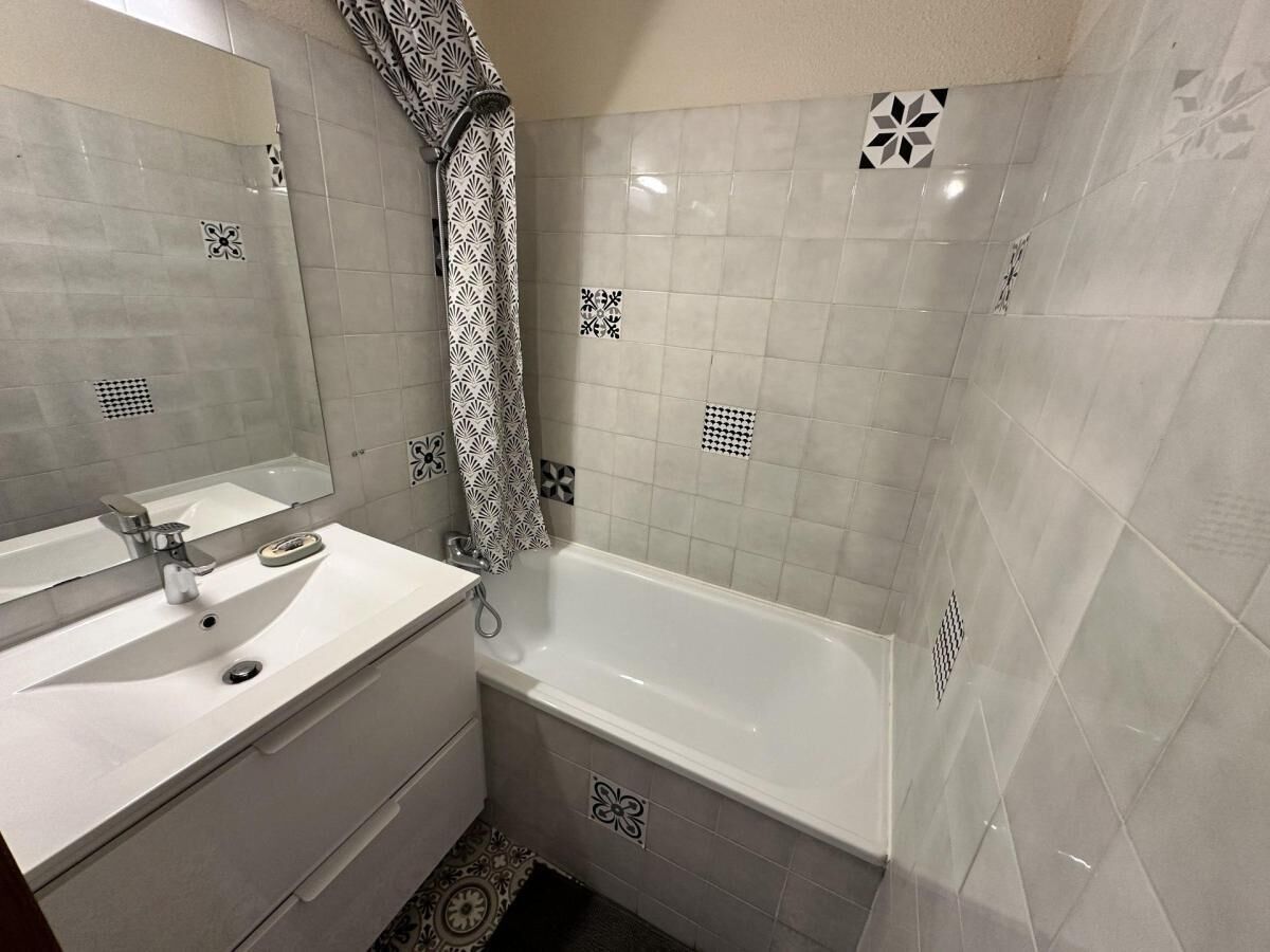 A bathroom with a white sink, mirror, and bathtub. There are patterned tiles on the walls and floor.