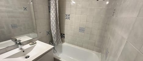 A bathroom with a white sink, mirror, and bathtub. There are patterned tiles on the walls and floor.