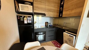 Cocina compacta con microondas, horno y lavavajillas. Hay una mesa de comedor con sillas y una alfombra pequeña.