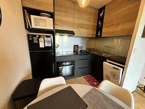 A compact kitchen with a microwave, oven, and dishwasher. There is a dining table with chairs and a small rug.