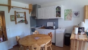 A compact kitchen with white cabinets, a small oven, a washing machine, and a dining table with chairs.