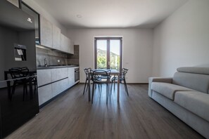 Μια σύγχρονη κουζίνα με τραπεζαρία, έναν καναπέ και ένα μπαλκόνι με θέα στους λόφους.