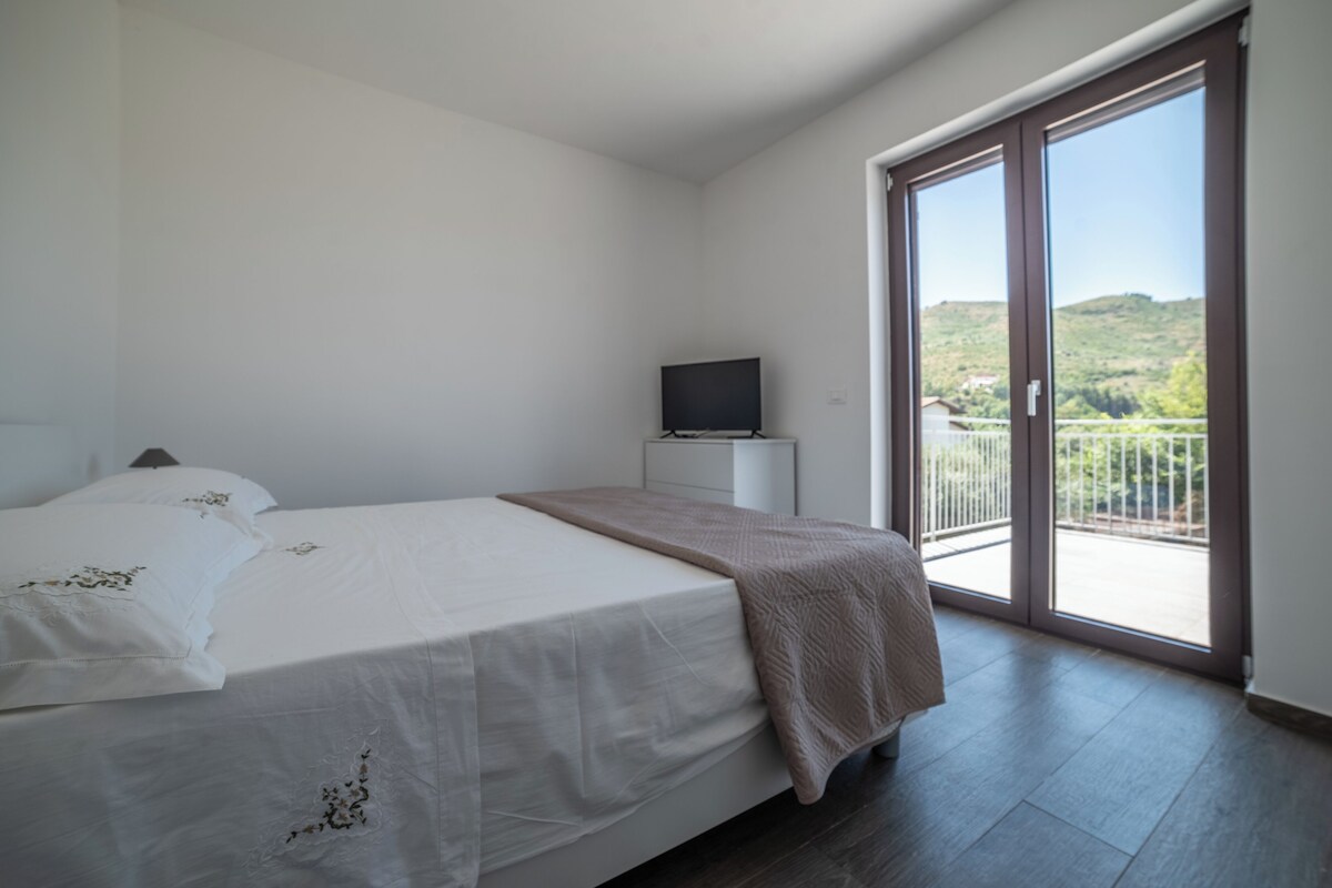 Une chambre à coucher avec un lit, un téléviseur posé sur un meuble et un balcon donnant sur un paysage verdoyant.