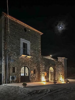 A stone building with a balcony and an arched entrance, illuminated by exterior lighting. - Casa Vacanze Signora Cinzia (Torchiara)