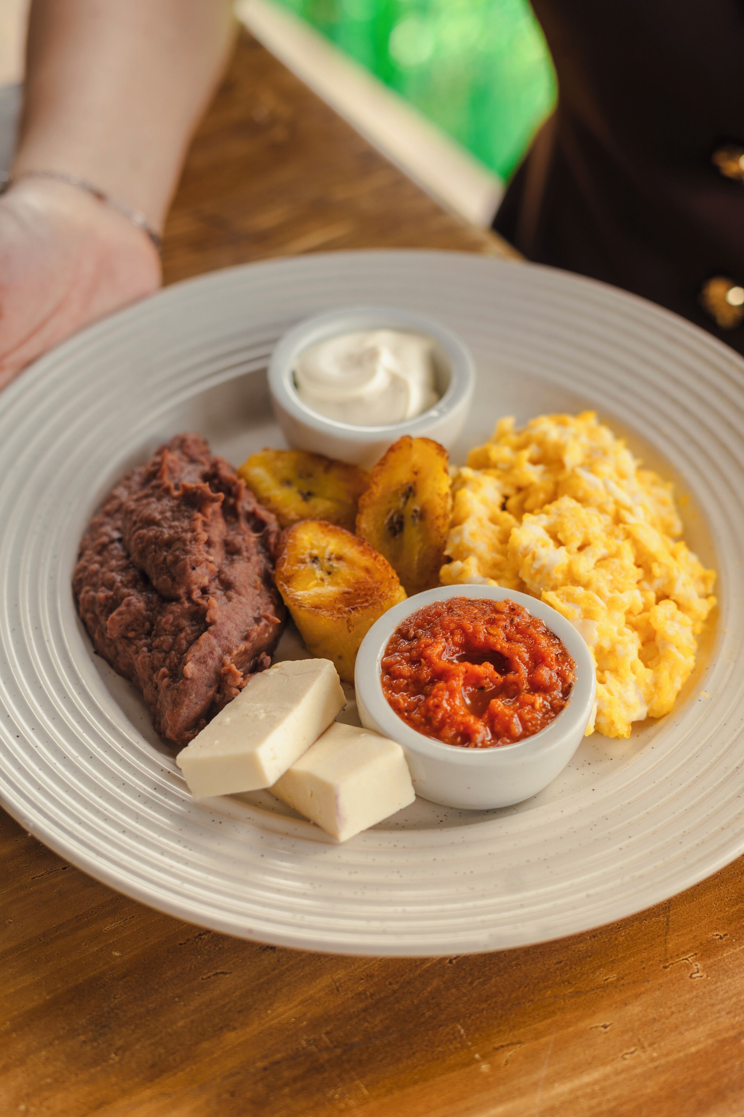 Een bord met bonen, gebakken plantains, roerei en twee kleine schaaltjes saus.