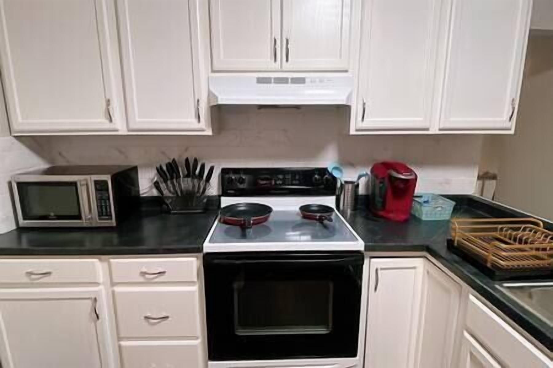 A kitchen with white cabinets, a microwave, a stove, and a coffee maker.