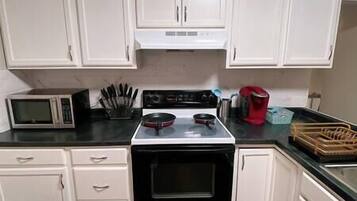 A kitchen with white cabinets, a microwave, a stove, and a coffee maker.