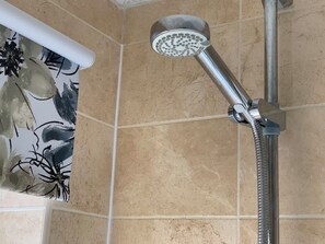 A showerhead with a flexible hose, mounted on a wall with beige tiles. - Rhubarb Cottage, stylish home close to Lyndhurst High street & New Forest trails (Lyndhurst)
