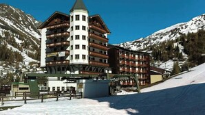A multi-story hotel with a central tower, ski lift, and snow-covered mountains in the background. - Hotel Adler (Foppolo)