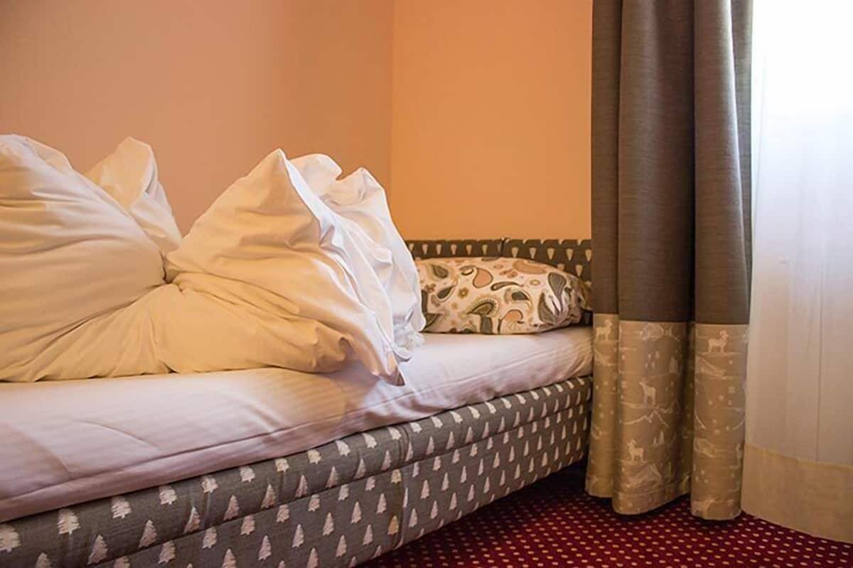 A bed with white and patterned pillows, grey patterned bedding, and grey curtains.